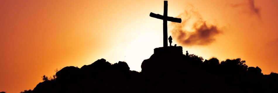 human standing beside crucifix statue on mountain