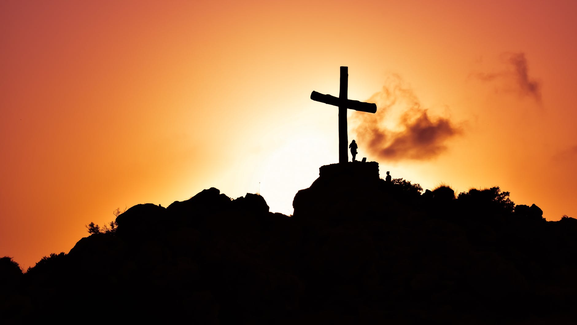 human standing beside crucifix statue on mountain